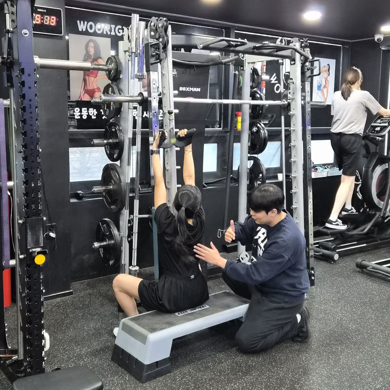 랙 앞에서 트레이너가 회원의 운동을 지도하는 장면
